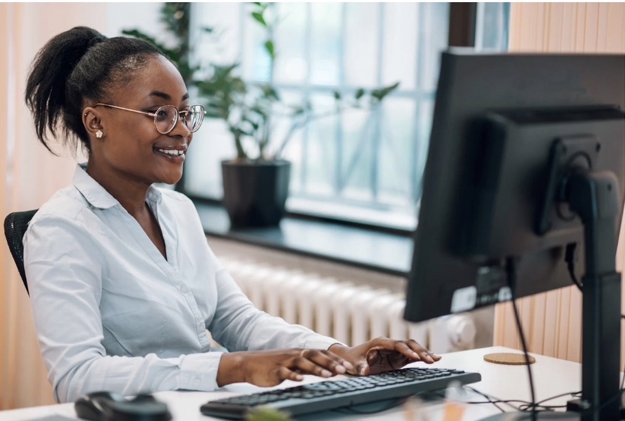 Young professional woman smiling at her workstation in a bright, plant-filled office.